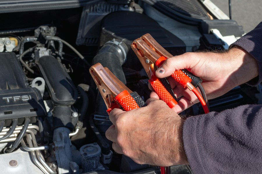 Mechanic holding red and black jumper cable clamps over an engine